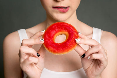 Midsection of woman holding donut against gray background