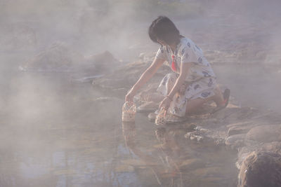 Side view of woman kneeling by hot spring