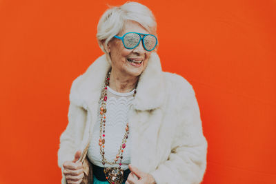 Fashionable senior woman standing against wall