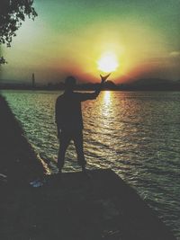 Rear view of silhouette man fishing in sea against sunset sky