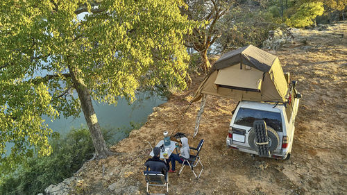 Aerial view of a couple camped with their jeep and rooftop tent and having breakfast at riverside, cunene river area, angola