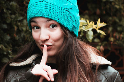 Close-up portrait of young woman with finger on lips against plants during winter