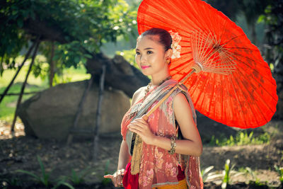 Smiling beautiful young woman wearing traditional clothing while holding red umbrella