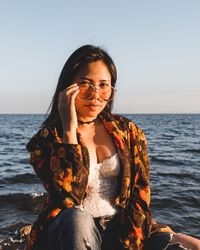 Portrait of young woman in sunglasses sitting at beach