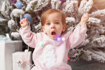 Portrait of cute girl holding christmas lights while sitting at home
