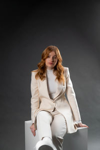 Portrait of young woman sitting against black background