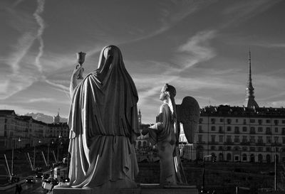 Statue in city against cloudy sky