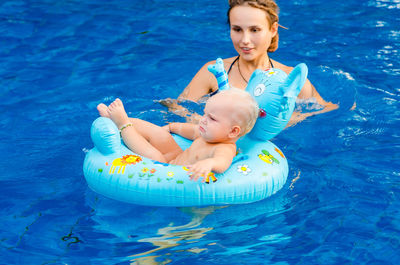 Woman with baby boy on inflatable ring swimming in pool