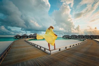 Rear view of woman standing on pier over sea against sky