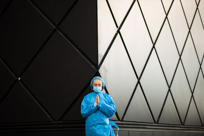 Young woman wearing mask standing against wall