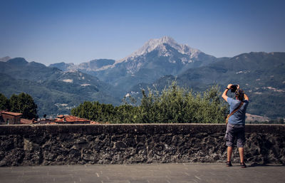 Rear view of man photographing on mountain against sky