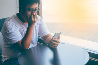 Midsection of man using mobile phone while sitting on table