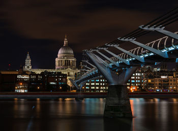 Illuminated bridge over river and buildings in city at night