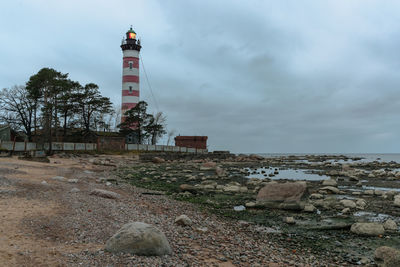 Lighthouse amidst rocks and buildings against sky