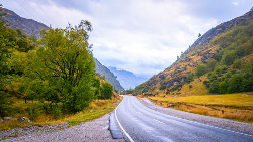 Road amidst trees and mountains against sky