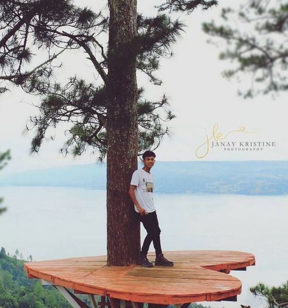 PORTRAIT OF MAN STANDING ON TREE TRUNK BY SEA