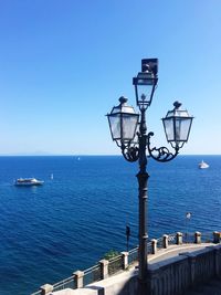 Street light by sea against clear blue sky