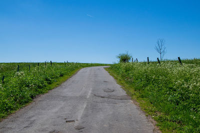 Road amidst field against clear blue sky