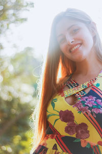 Portrait of smiling young woman standing against trees