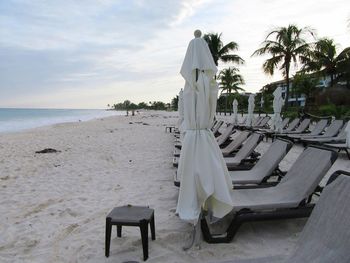 Deck chairs on beach against sky