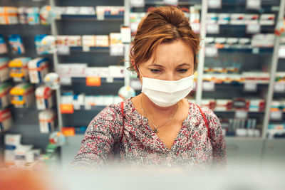 Woman shopping at pharmacy, buying medicines, wearing face mask to cover mouth and nose