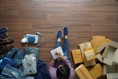 Directly above view of businesswoman sitting amidst clothes and cardboard boxes on hardwood floor