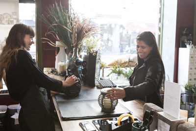 Smiling female customer looking at lantern while standing in front of young owner