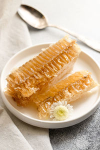 Sealed honeycomb of honey with little spoon on a white porcelain plate on a grey table