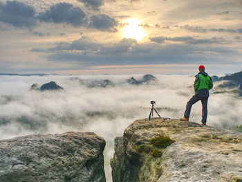 Professional artist on cliff. nature photographer takes photos with digital camera on peak of rock. 