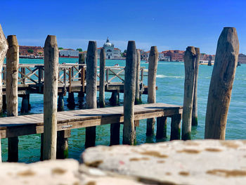 Wooden post on pier by sea against clear blue sky