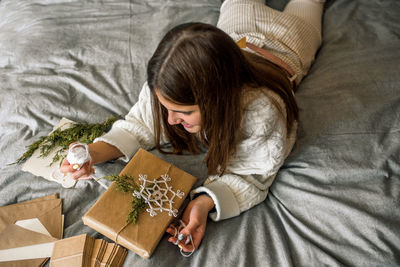 High angle view of girl decorating gift box while lying on bed