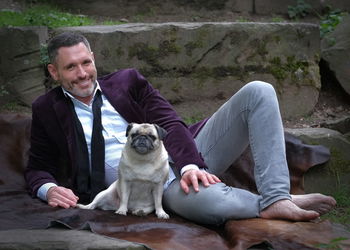 Man with white-black bulldog on a dark brown fur. 