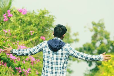 Rear view of man with arms outstretched against plants