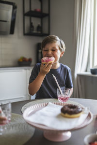Boy eating doughnut at table in living room