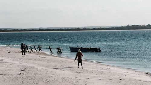 People pulling rope tied to boat in sea against sky