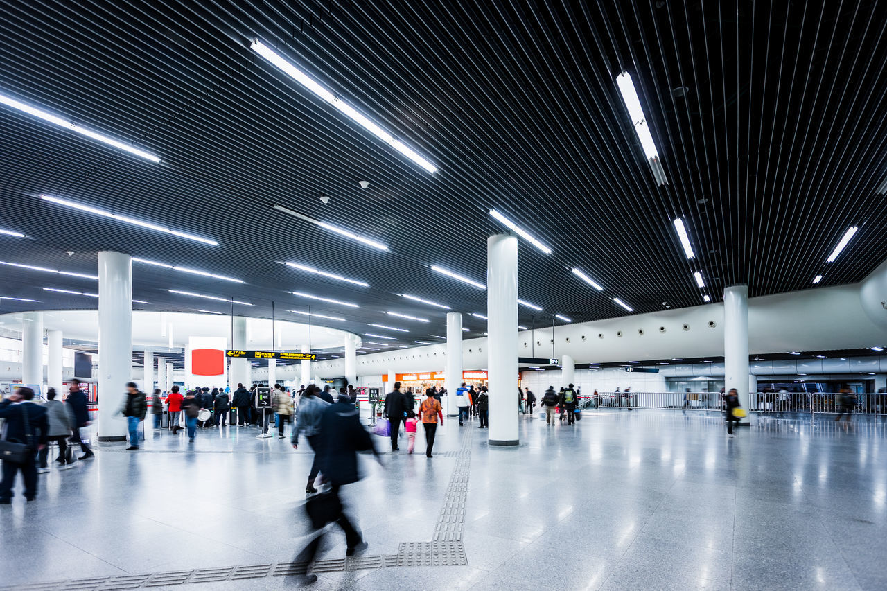 GROUP OF PEOPLE WALKING IN ILLUMINATED AIRPORT