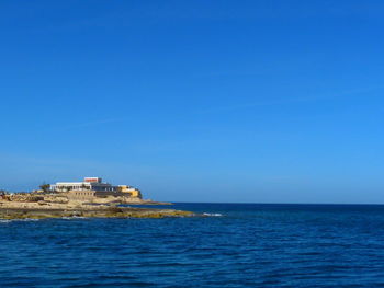 Building by sea against clear blue sky