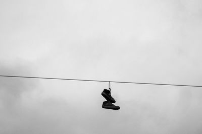 Low angle view of shoes hanging on cables against sky