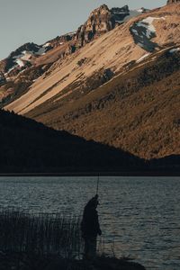 Man fishing on rock by lake against sky