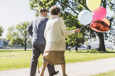 Back view of senior couple with balloons strolling in a park