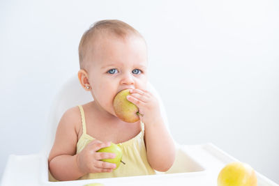 Portrait of cute baby boy eating apple in bathtub against white background