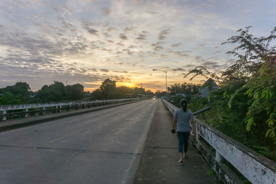 Rear view of woman on road against sky during sunset