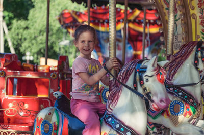 Smiling girl sitting on carousel at amusement park