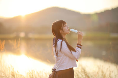 Side view of young woman standing by lake