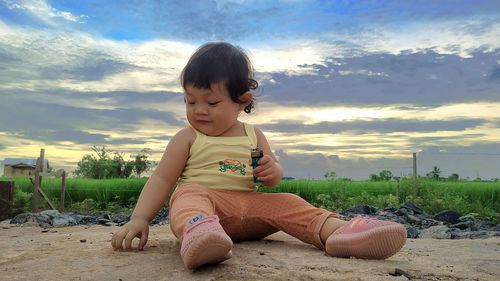 Cute boy sitting on land against sky during sunset