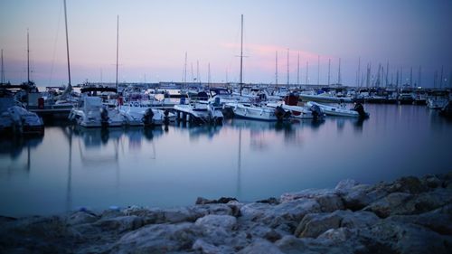 Sailboats moored on harbor against sky during sunset