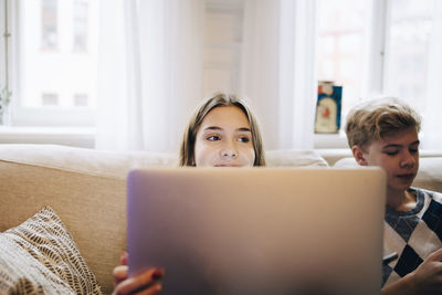 Girl using laptop while sitting with friend on sofa at home