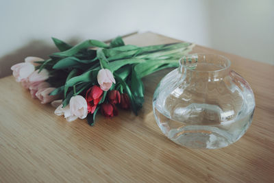 Pink red tulips lying by large glass vase with water. still life with flowers on table in room. 