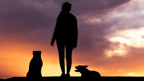 Silhouette man and woman standing against sky during sunset