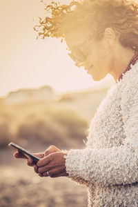 Young woman using mobile phone against sky during sunset